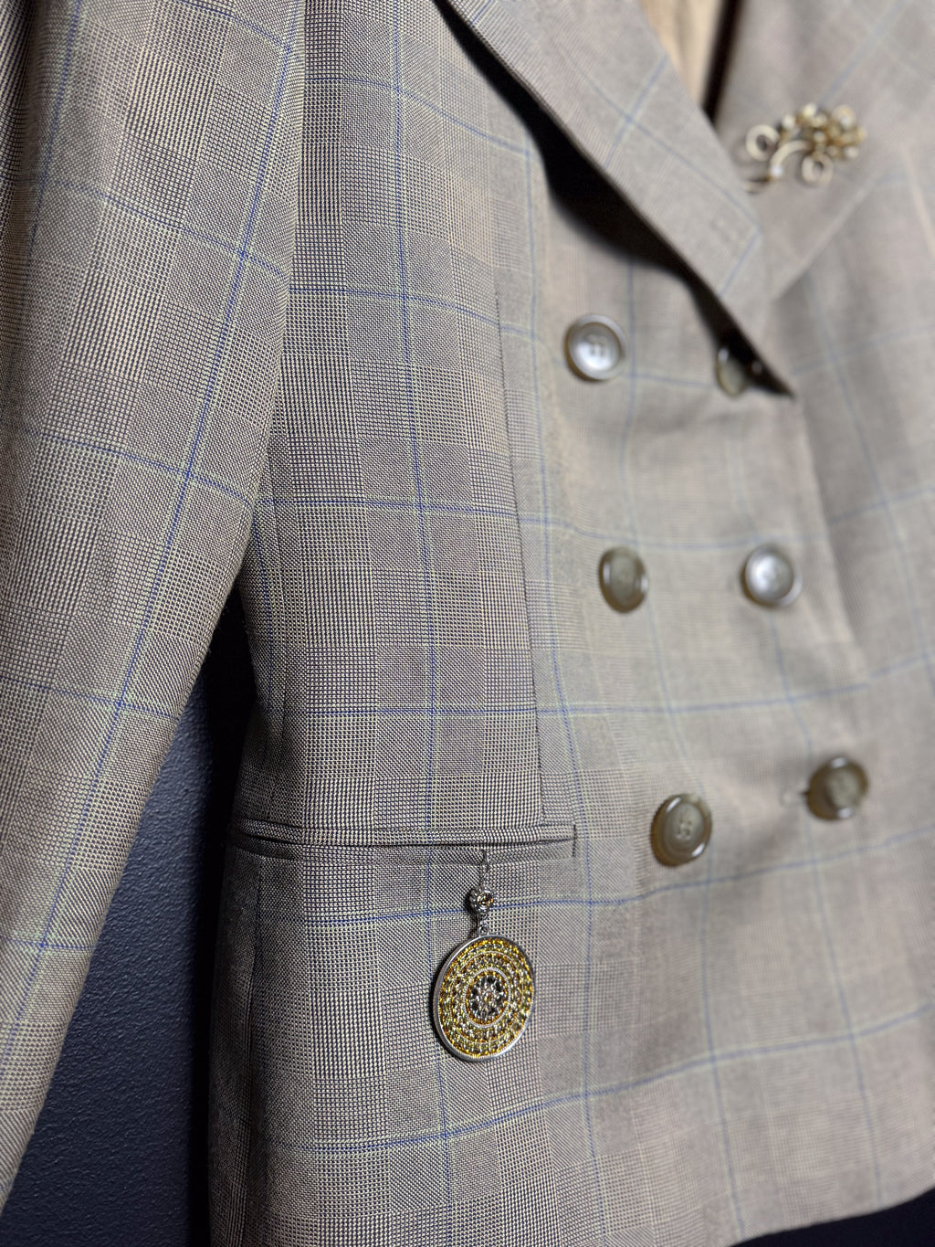 Close-up of a gray checkered suit jacket with buttons and a decorative pendant.