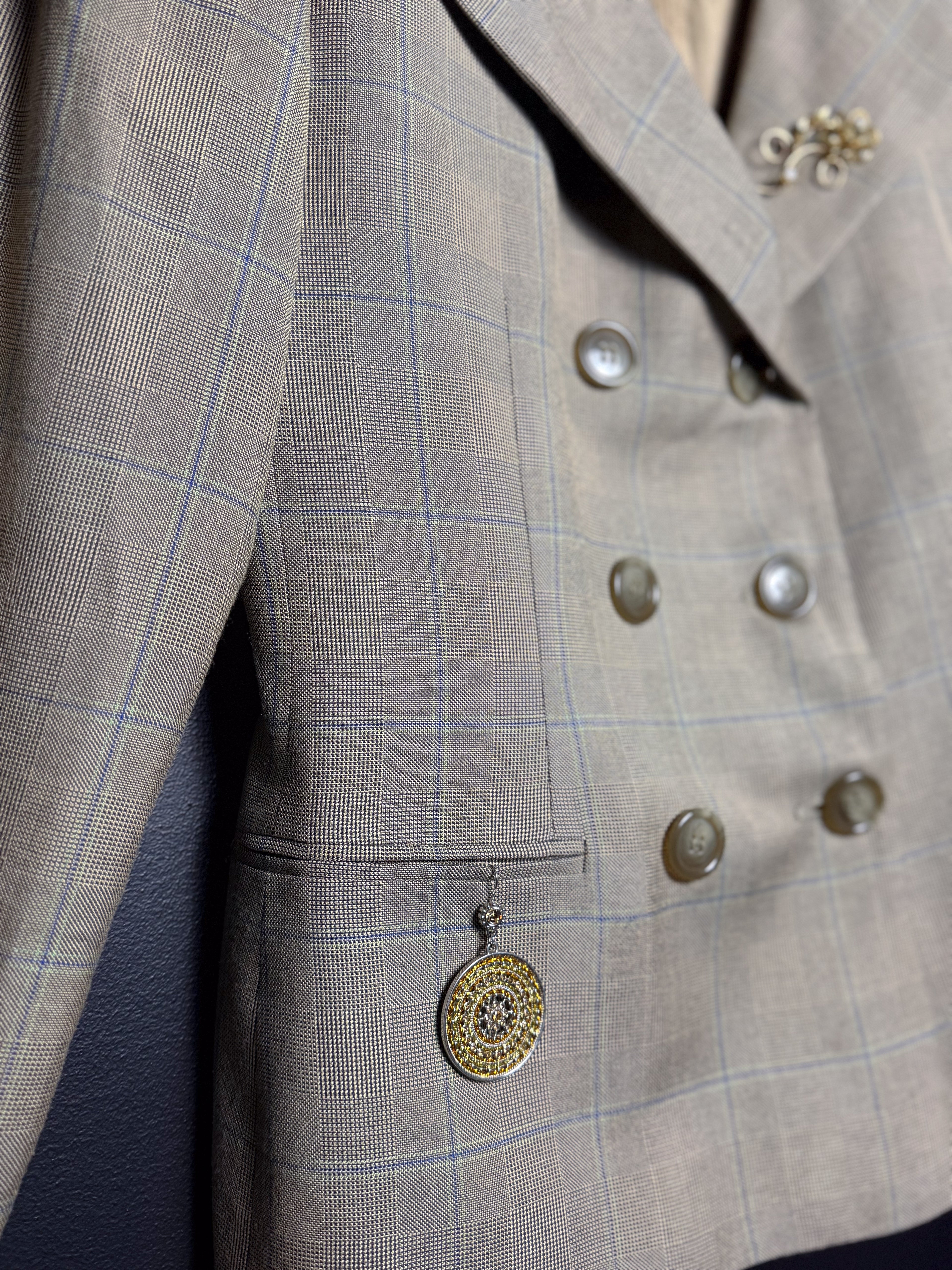 Close-up of a gray checkered suit jacket with buttons and a decorative pendant.
